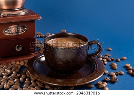 Cup with coffee and manual coffee grinder with coffee beans on a blue background. Photo