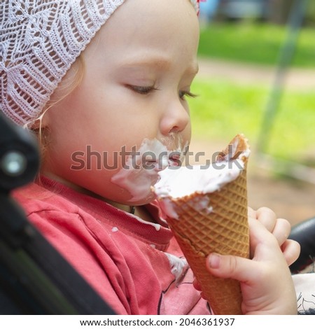 Cute little girl 2 years old eats sweet ice cream in the park and smeared her mouth and face with sticky ice cream.
