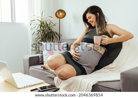Pregnant woman sitting on sofa using laptop. Concept of pregnant woman working from home