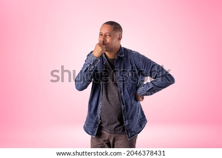 Man in short clothes wearing denim shirt, white t-shirt and brown pants in studio photo on a background with lights.