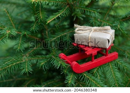 christmas red sled with gift in craft paper with ribbon on green fir tree, christmas backgrounds with free copy space