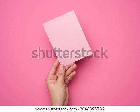 Female hand holding empty pink paper on a pink background. Copy paste image or text, close up