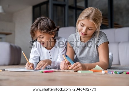 Two school age kids doing their homework on floor at home. Brother and sister siblings children drawing together, preparing for school lesson. Homeschool concept. Royalty-Free Stock Photo #2046402773