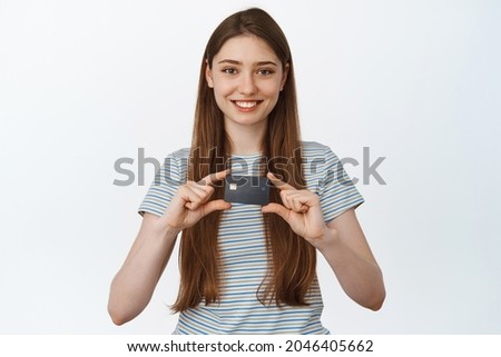 Bank and people concept. Smiling happy woman showing credit card in hands, standing in tshirt over white background