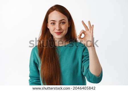 No problem, very well. Smiling young woman with red long hair, look satisfied, make okay zero sign, approve good thing, like and recommend, white background