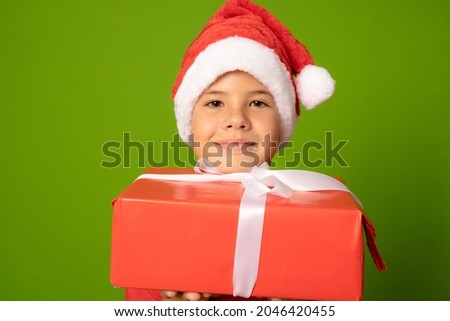 Smiling beautiful child in Santa red hat holding Christmas gift in hand. Christmas concept.