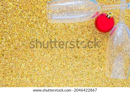 Two champagne glasses are lying in the corner of the picture, between them is a red Christmas ball on a gold textured background. top view, flat lay, copy space, isolate.