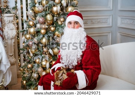 Santa Claus holds a gift in mittens on a Christmas tree, festive mood