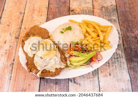 Tray of Ecuadorian churrasco with beef steak, fried egg on top and various garnishes of French fries, white rice and avocado with purple onion salad Royalty-Free Stock Photo #2046437684
