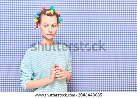 Portrait of thoughtful young woman without makeup with colorful hair curlers on head, looking melancholic and dreamy, standing over shower curtain background, with place for your text and design Royalty-Free Stock Photo #2046448085