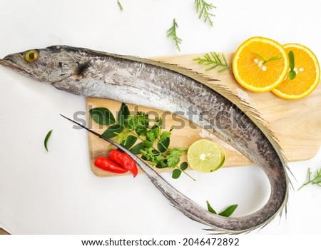 Fresh Largehead hairtail fish,Belt fish decorated with herbs and vegetables on a wooden pad.Selective focus.