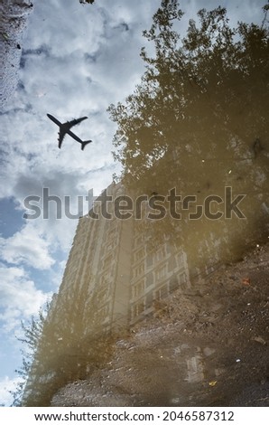 Reflection of a building and a flying plane in a puddle on the asphalt after a rain. Abstract photography.