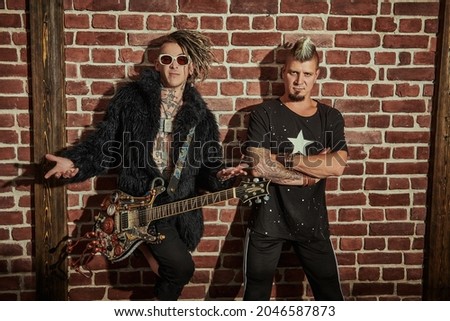 Two punk rock musicians in concert costumes posing with an electric guitar near a brick wall. Youth alternative culture. Grunge style.  Royalty-Free Stock Photo #2046587873