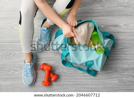 Woman in sport shoes preparing bag for training on light wooden floor Royalty-Free Stock Photo #2046607712