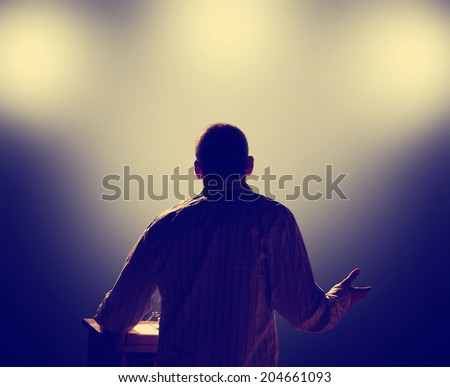 a young man in front of a podium and an audience Royalty-Free Stock Photo #204661093