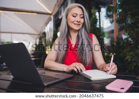 Photo of mature attractive asian woman happy positive smile write pen notes to-do plan laptop virtual restaurant outdoors