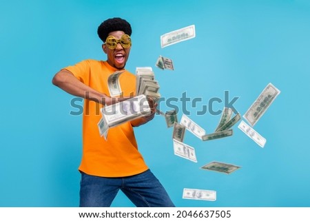 Photo of crazy happy dark skin young man hold hands money fly air wear sunglass isolated on blue color background