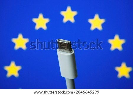 Concept for EU law to force USB-C chargers for all phones. EUROPEAN UNION flag and USBC universal charging cable. Selective focus. Royalty-Free Stock Photo #2046645299
