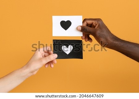 Hands of Caucasian woman and African-American man holding paper sheets with drawn heart on color background. Racism concept Royalty-Free Stock Photo #2046647609