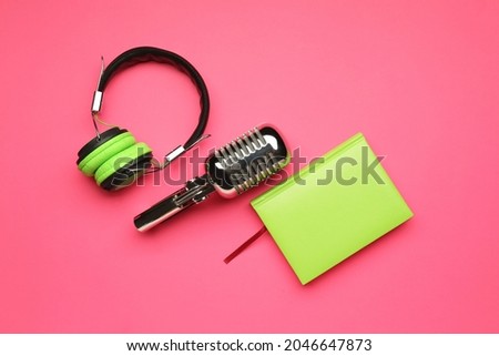 Headphones with microphone and notebook on color background