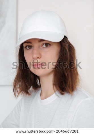 Female model wearing a white baseball cap. White cap mockup, template for picture, text or logo. Girl holding visor of cap. Free space, copy space.