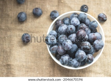 Ripe sweet plums in a deep white plate on burlap