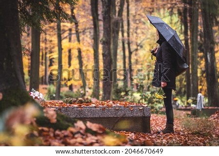 Silent grief in graveyard. Lone sad woman mourning for dead person at grave in cemetery. Mourner with umbrella in rain Royalty-Free Stock Photo #2046670649