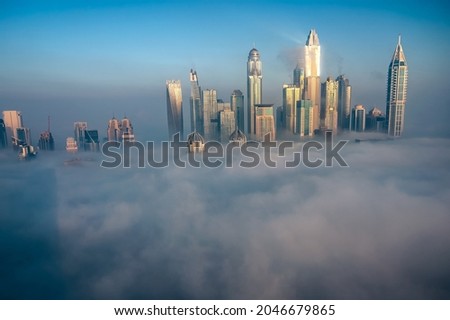Skyscrapers of Dubai Marina covered in thick fog. Day time picture with blue sky. 