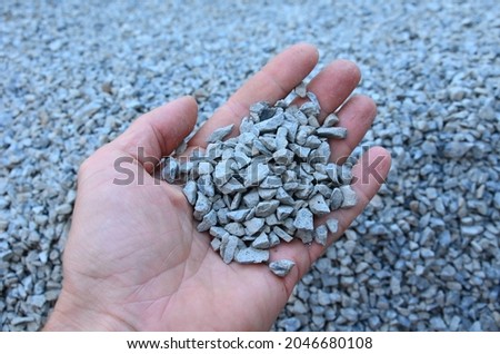 man holds in his hand a sample of stone gravel or pebbles of one size. Marble white gravel and gray brown pebbles straight from the quarry. Royalty-Free Stock Photo #2046680108