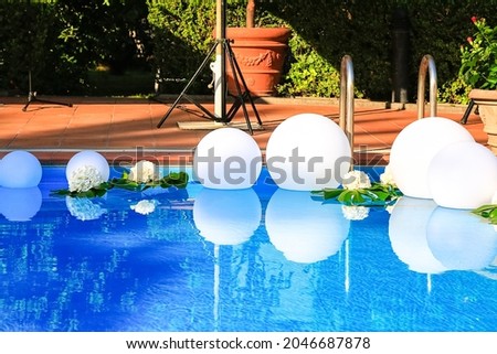 Open air swimming pool decorated with white floating balls and fresh flowers for wedding party. Summer event preparation. Party design. Clean transparent blue water. Background and postcard picture 