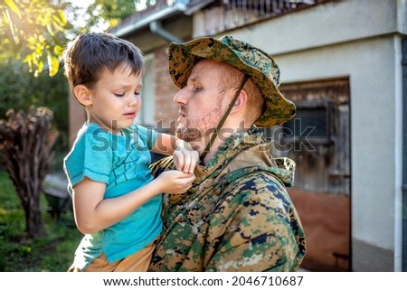 Cropped shot of a sad son hugging father in military uniform on bright background. Photo of young soldier man saying goodbye to his son. 