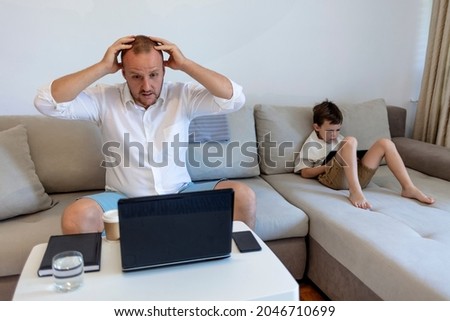 Shot of upset young working father taking care of his small son and working from home during the day. Businessman working at home. A cute little boy looking at tablet while dad tightly working.