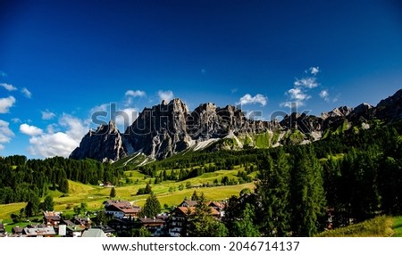 A scenic shot of the Cortina d'Ampezzo town fields and rocky ski mountain under a cloudy sky in Italy