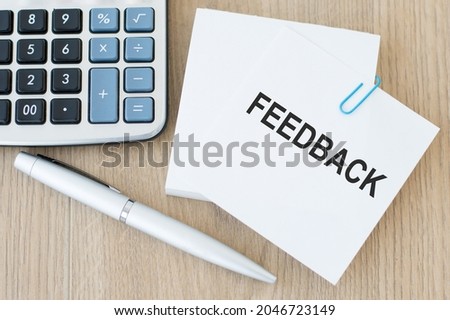 White card with text Feedback stands on the desk next to calculator and pen