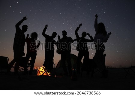 Group of friends having party near bonfire in evening. Camping season