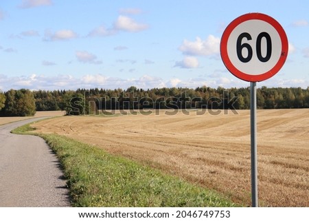 Speed limit 60 sign in the middle of a beautiful country road, golden fields and blue sky with cute fluffy clouds. Gorgeous nature scenery. 
