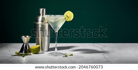 Martini glass with cocktail or mocktail and lime wedge, shaker and jigger on dark background. Long wide banner