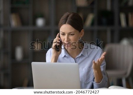 Angry businesswoman talking on phone, looking at laptop screen, irritated young woman arguing with customer client, having unpleasant conversation, holding smartphone, solving business problem Royalty-Free Stock Photo #2046772427