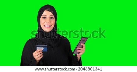 online shopping and paying bills at home. Smiling young cute Arabic female makes purchase in online store, holds credit card, isolated on green background, free space.