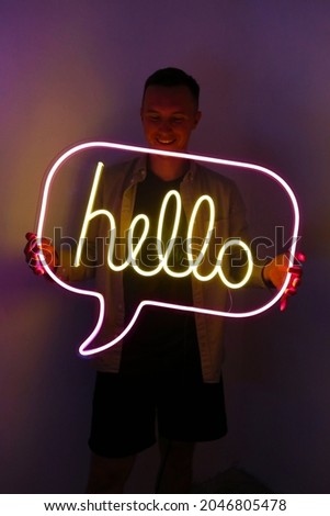 Handsome young man holding pink and yellow neon sign hello.  Trendy style. Neon sign. Custom neon. Home decor.