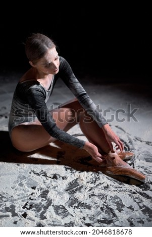 graceful elegant woman ballerina in pointe and gymnastic costume sitting on floor with flour resting after exhausting training, taking pointe shoes off. caucasian ballerina relaxing alone