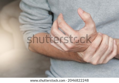 A man holding hand tight on wrist with pain, paralysis, numbness caused by repeatedly work, long-term use. Carpal tunnel syndrome concept. Light effect, selective focus.