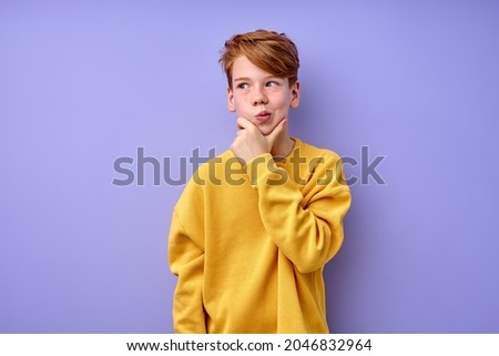 Let me think. Thoughtful clever redhead schooler in yellow shirt with puzzled serious expression, child thinking doubting, making choice. indoor studio shot isolated on purple background Royalty-Free Stock Photo #2046832964
