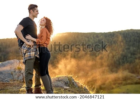 Female and male hikers walking in summer mountains in countryside. Happy couple talking together. Redhead curly woman and handsome man in casual wear travelling, enjoy nature. people lifestyle
