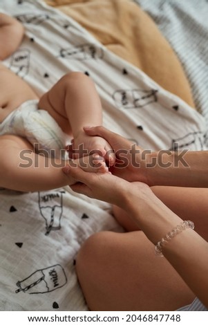 Cropped photo baby's feet in female hands. Top view unrecognisable woman holding newborn's feet in her hands. Physical excercises for babies. Healthy childhood concept.