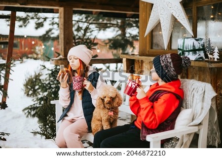 two children boy and teenage girl with poodle dog sitting on porch of village house and drinking hot chocolate with croissants during Christmas winter holidays, Christmas and New year vacation concept