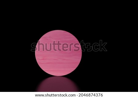 Close-up pink round textured wooden shape on black background with reflection.Low key.Copy space for text.Product placement room.Horizontal banner.Minimalism.Concept of supermoon or sun in darkness