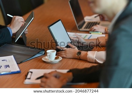 Cropped image of business people's hands is using a computer laptop and digital tablet during the meeting at the wooden office desk.