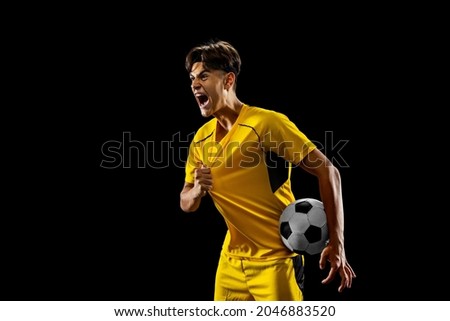 After winning game. Happy proud male football player in yellow uniform isolated over dark background. Successful competition. Concept of action, speed, energy, sport, competition and ad. Royalty-Free Stock Photo #2046883520