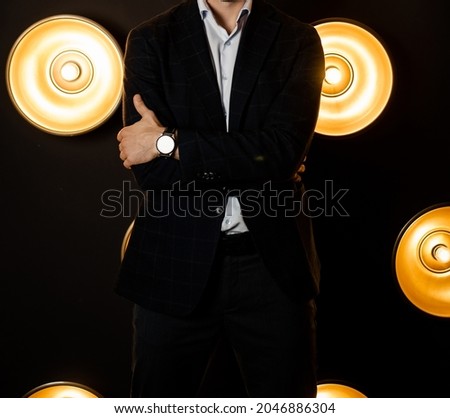 Stylish fashionable unrecognizable man in a jacket in a white shirt in a dark room with lamps.